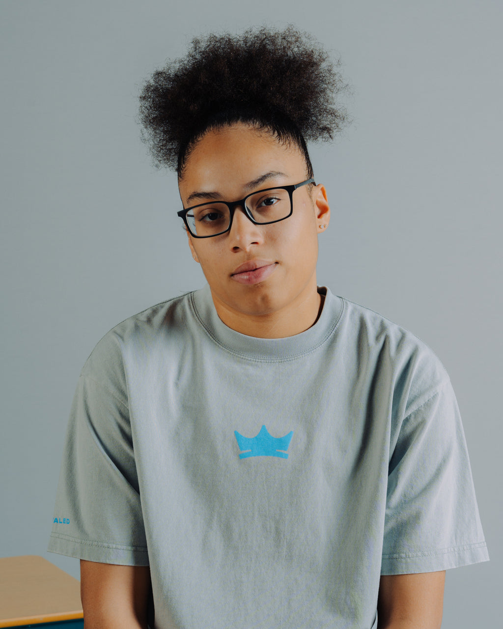 Olivia Miles wearing a gray t-shirt with a blue Unrivaled crown logo on a plain background