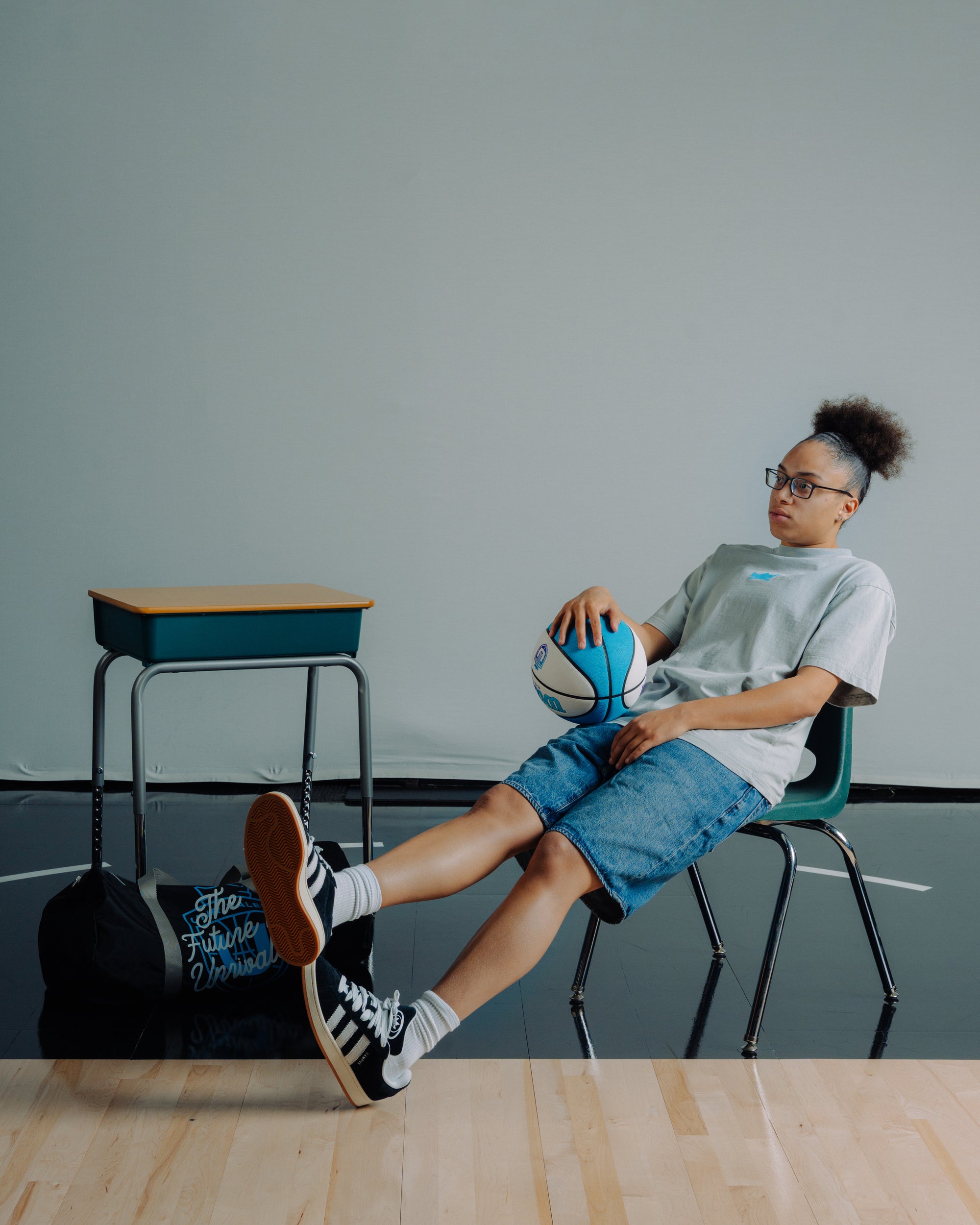 Olivia Miles leaning back with a large XL gym bag on the floor.