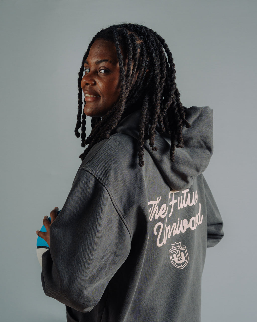 Milaysia Fulwiley turning toward the camera showing the back of a washed black Unrivaled hoodie with text that says "The Future Is Unrivaled"