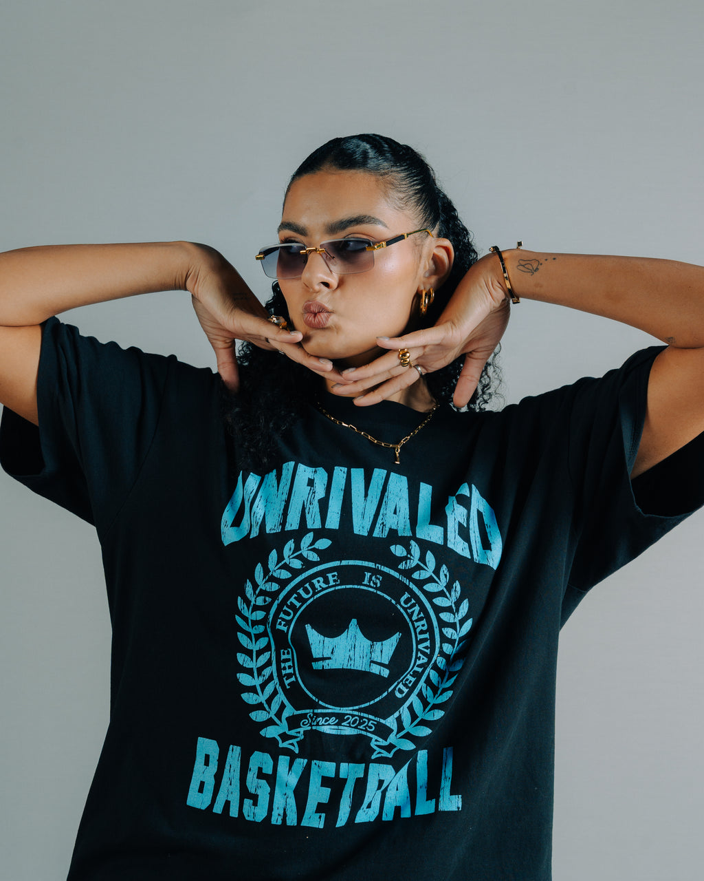 Lauren Betts framing her face with her hands and wearing a black shirt with blue text that says Unrivaled Basketball 