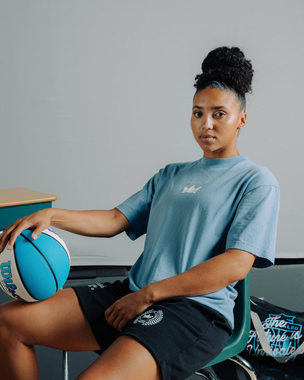 Azzi Fudd sitting with a Wilson Unrivaled basketball with a blue crown shirt, and black athlete Unrivaled shorts