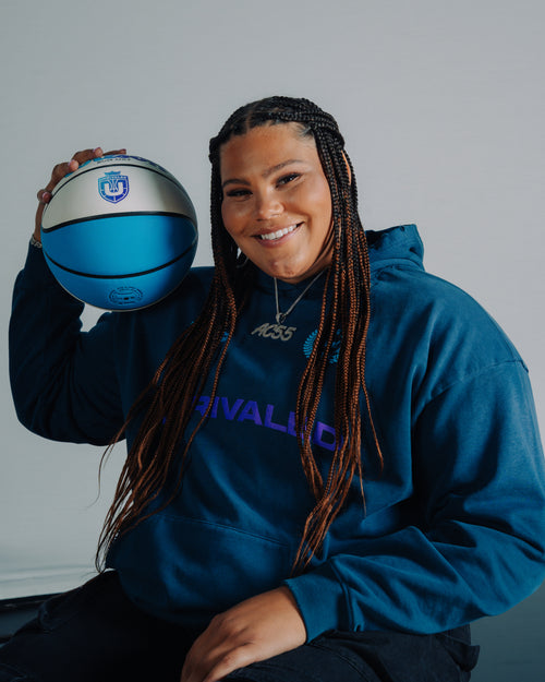 Audi Crooks posing in a blue hoodie holding a Wilson Unrivaled Basketball on her shoulder. 